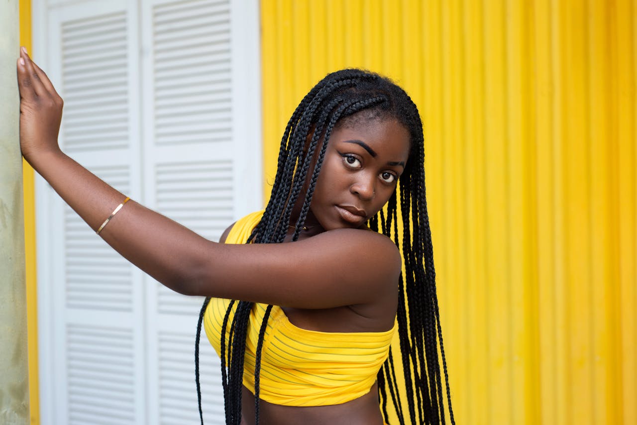 Stylish portrait of a woman with braided hair in yellow outfit and wall.