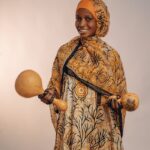 Portrait of a woman smiling while holding traditional African shakers.